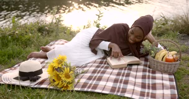 身穿白衣的黑人妇女在河边看书 — 图库视频影像