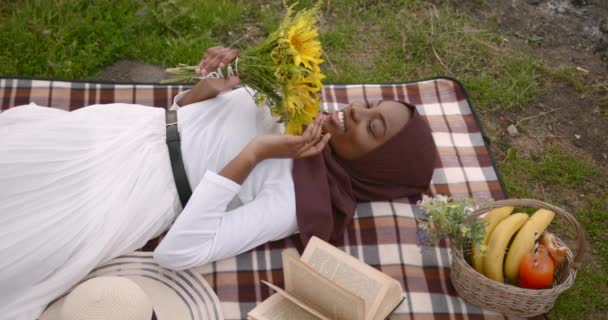 Sort kvinde med blomster liggende på picnic tæppe – Stock-video