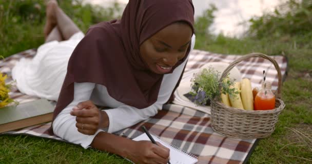 Müslüman bir kadının portresi nehir kenarındaki ekoseli piknik battaniyesinde yatıyordu. — Stok video