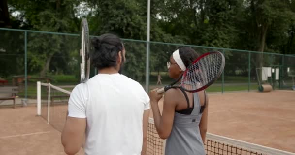 Πολυεθνικός άνδρας και γυναίκα στα αθλητικά μιλώντας για τένις στο γήπεδο — Αρχείο Βίντεο