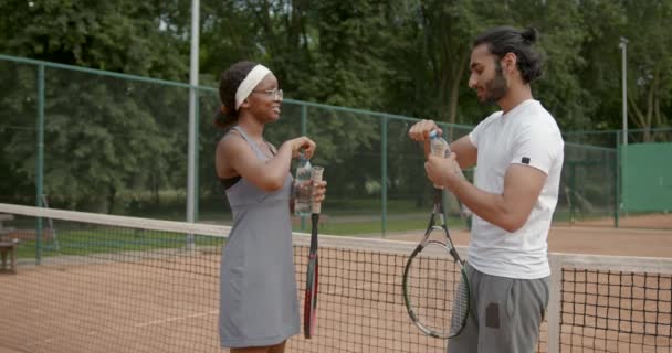 Multi ethnic couple drink water after tennis match — Stock Video