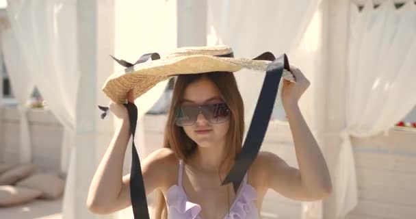 Young girl putting on straw hat at resort — Stock Video