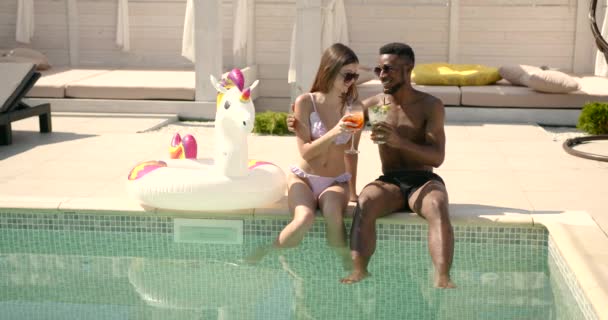 Amis multiraciaux assis au bord de la piscine avec cocktails — Video