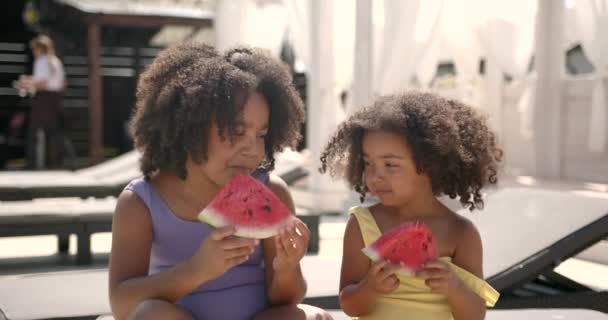 Dwa słodkie dziewczyny jedzące arbuza na leżakach na basenie — Wideo stockowe
