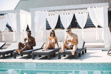 Mayolu üç arkadaş yüzme havuzunun yanında kokteyl içerek rahatlıyor.