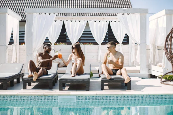 Tres amigos en un baño se relajan con un cóctel cerca de la piscina — Foto de Stock