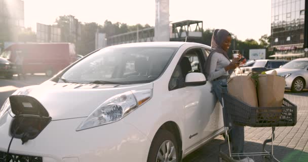 Femeia musulmană africană încarcă mașina și folosește telefonul — Videoclip de stoc