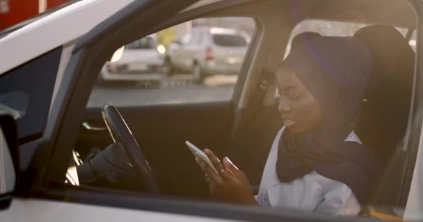 Чорношкіра мусульманка використовує планшет у білій машині — стокове відео