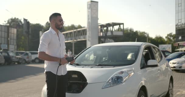 Mladý Arab muž dobíjení bílé elektrické auto na parkovišti — Stock video