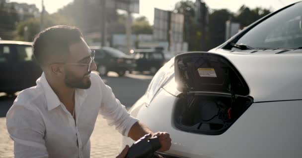 Mladý Arab muž dobíjení bílé elektrické auto na parkovišti — Stock video
