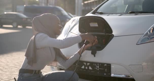 Černá muslimská dívka nabíjení elektro auto na nádraží — Stock video