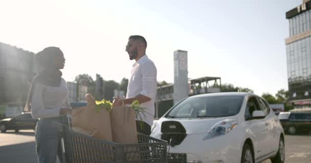 Multi coppia etnica carica auto elettrica dopo lo shopping — Video Stock