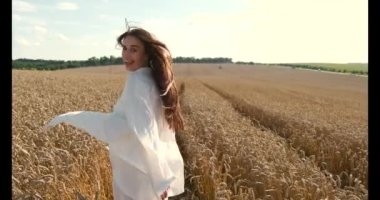 Beyaz elbiseli genç esmer kadın buğday tarlasında yürüyor.