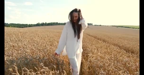Молодая брюнетка в белой одежде ходит по пшеничному полю — стоковое видео