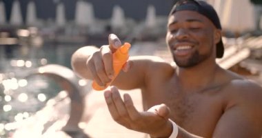 Siyah genç adam tatil köyünün havuzuna güneş kremi sürüyor.