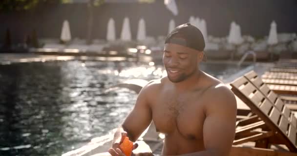 Jeune homme noir mettant de la crème solaire à la piscine de la station — Video