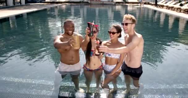 Fyra vänner klamrar sig fast med cocktails vid poolen — Stockvideo
