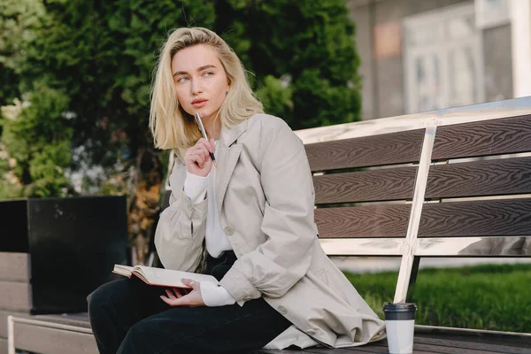 Rubia sentada en un banco con cuaderno — Foto de Stock