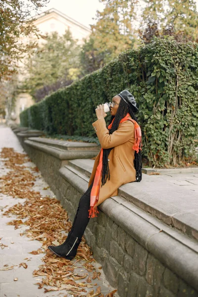 Молода чорна жінка в пальто п'є каву зовні — стокове фото