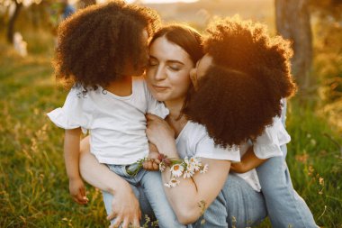 İki Afrikalı Amerikalı kız kardeş parkta beyaz annelerini öpüyor.