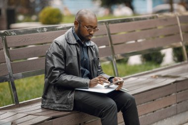 Siyah adam bankta oturuyor ve bazı notlar alıyor.