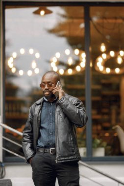 Siyah bir adam sokakta duruyor ve telefon kullanıyor.