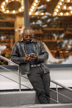 Siyah bir adam sokakta duruyor ve telefon kullanıyor.