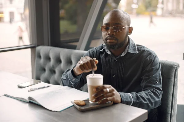 Uomo nero seduto in un caffè con una tazza di latte e carte — Foto Stock