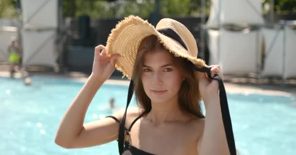 Bella ragazza brunnete in cappello di paglia sorridente alla fotocamera vicino alla piscina — Video Stock