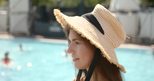 Frumos tineri bruneta fata în pălărie paie zâmbind la camera aproape de piscină — Videoclip de stoc