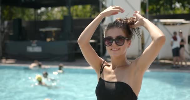 Een dame in badpak en een bril poseren bij het buitenzwembad — Stockvideo