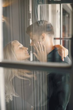 Romantik genç çift kafe vitrininde sarılıyor.