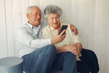 Zarif yaşlı çift evde oturuyor ve telefon kullanıyor.