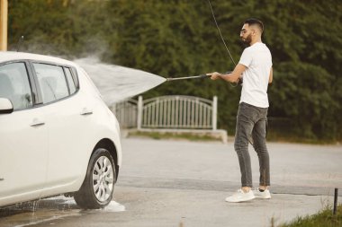 Hintli adam araba yıkamada beyaz aracını yıkıyor.