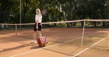 Elinde tenis topu olan bir kadın sahada yürüyor.