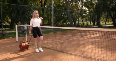 Elinde tenis topu olan bir kadın sahada yürüyor.