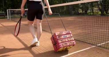 Elinde tenis topu olan bir kadın sahada yürüyor.