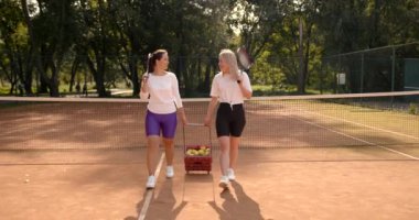 Sahada tenis topu taşıyan iki kadın.