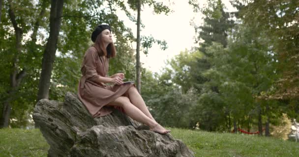 Flickkonstnär sitter barfota på en sten i parken — Stockvideo