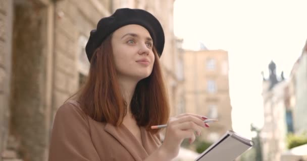Meisje kunstenaar met een notebook kijkt in de verte op de straat — Stockvideo