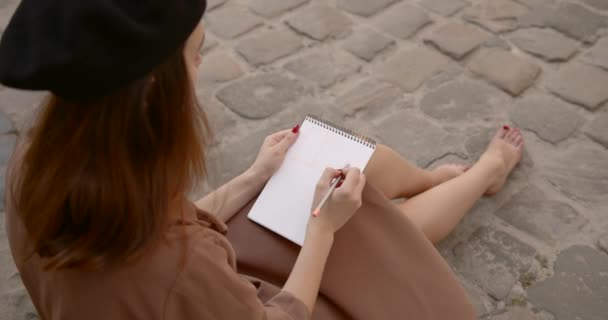 Künstlerin sitzt auf dem Bürgersteig und malt in Notizbuch — Stockvideo
