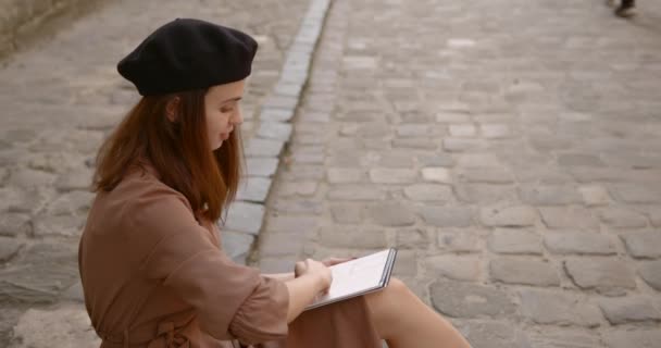 Menina artista senta-se na calçada e pinta em um caderno — Vídeo de Stock