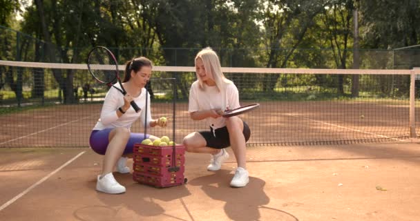 Δύο νεαρές γυναίκες κάθονται με κουτί για μπάλες του τένις — Αρχείο Βίντεο