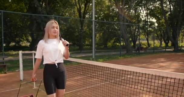 Mujer con caja de pelotas de tenis caminando por la cancha — Vídeos de Stock