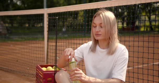 Kobieta pije wodę siedząc na korcie tenisowym — Wideo stockowe