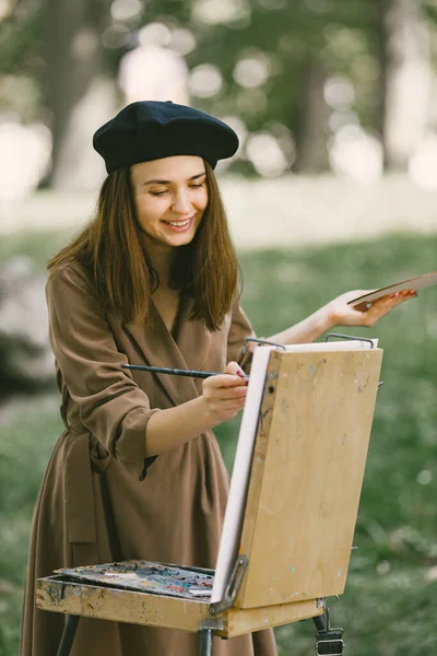Ragazza in abito e cappello nero pittura su un cavalletto in un parco — Foto Stock