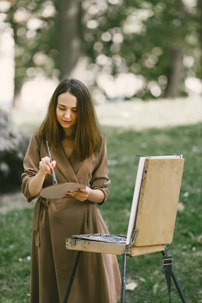 Girl in dress painting on an easel in a park barefoot — Stock Photo, Image