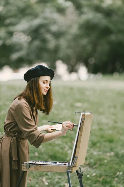 Parktaki sehpada resim yapan siyah şapkalı bir kız. — Stok fotoğraf