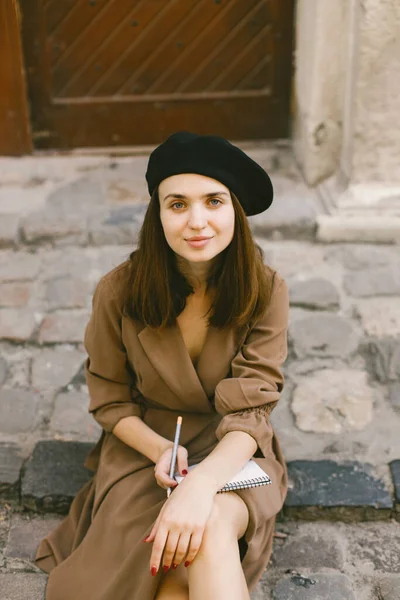 Portrét dívky v šatech a černý klobouk malování náčrt, zatímco sedí na ulici — Stock fotografie