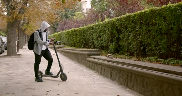 Hombre negro de pie en un scooter eléctrico con un teléfono — Vídeo de stock